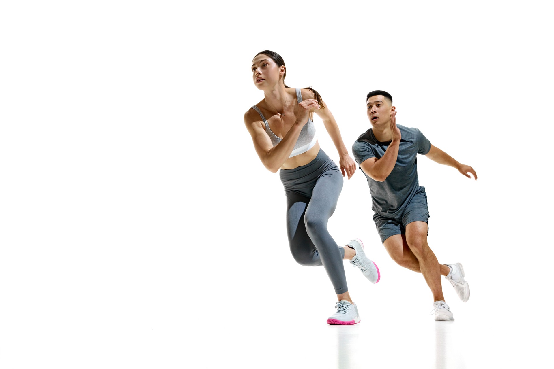 Man and woman wearing sports clothes mid-stride during sprinting exercise against white studio background. Teamwork.